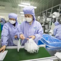 People work on a production line at a factory for medical masks in Haian, in eastern China\'s Jiangsu Province, in January.  | CHINATOPIX / VIA AP
