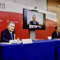 Yoshiro Mori (left), president of the organizing committee for the Tokyo Olympics and Paralympics, speaks during an online video news conference also attended by organizing committee CEO Toshiro Muto (right) and IOC Coordination Commission chair John Coates (on screen) on Thursday. | KAZ NAGATSUKA