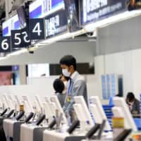 An employee, wearing protective mask amid the spread of COVID-19, works at a counter for All Nippon Airways (ANA) at the almost empty Kansai International Airport in Osaka in March. | REUTERS