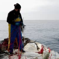 French fisherman Loic Barbedette gathers his net off the coast of Nice, France, on Thursday. The closure of restaurants and hotels, together with the difficulties of maintaining social distancing among crews at sea, have caused hundreds of fishing vessels to be tied up at ports around the world. | AFP-JIJI