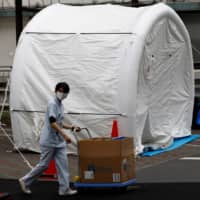 Medical workers walk by tents set up to test for the new coronavirus at Kawakita General Hospital in Tokyo on Friday. | REUTERS