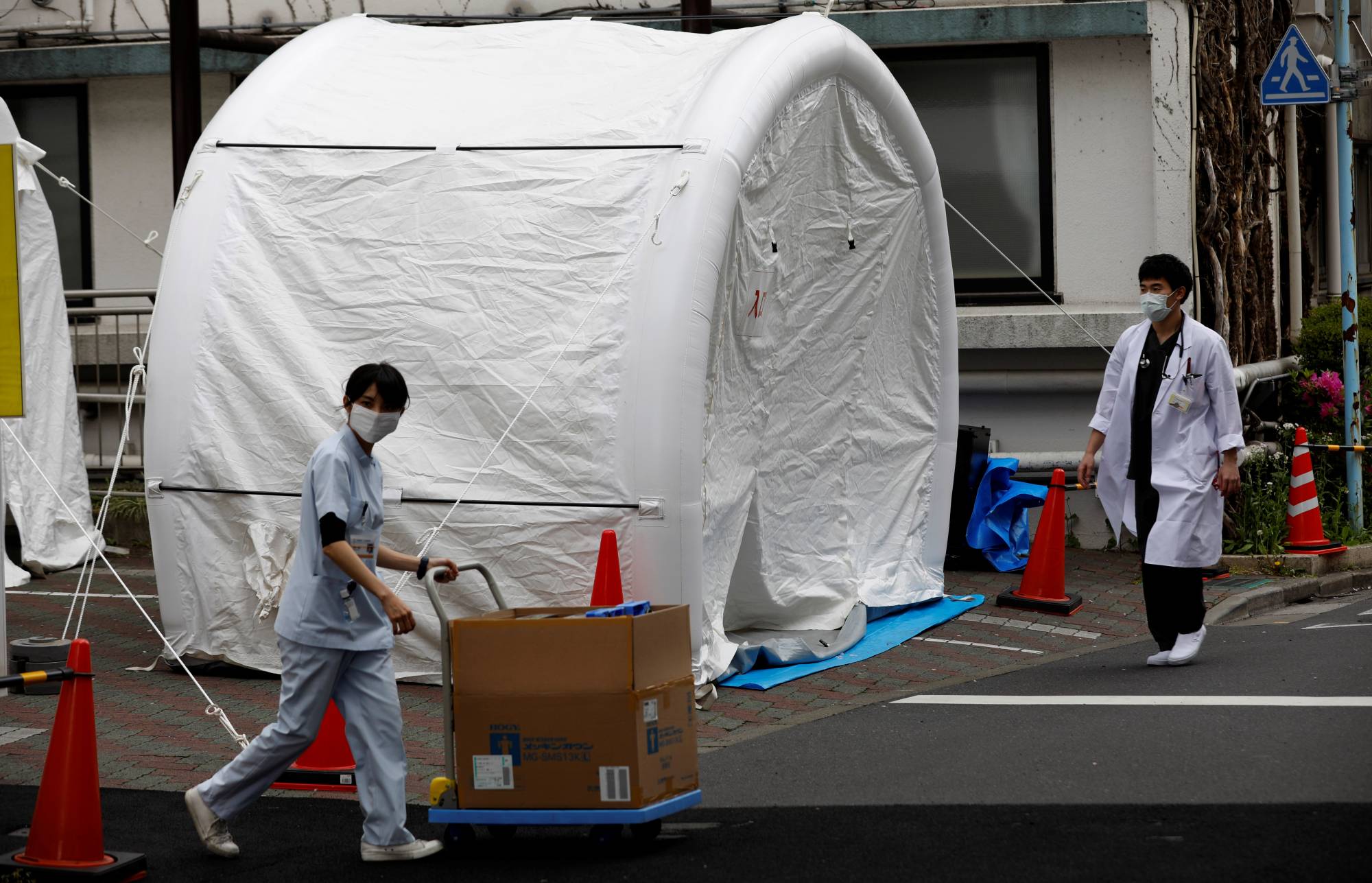 Medical workers walk by tents set up to test for the new coronavirus at Kawakita General Hospital in Tokyo on Friday. | REUTERS