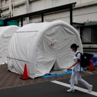 A medical worker walks by tents set up to test for the new coronavirus at Kawakita General Hospital in Tokyo on Friday. | REUTERS