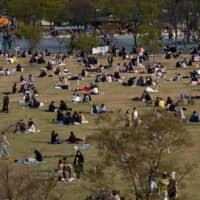 People wearing protective masks sit at a park near the Han River in Seoul on Saturday. | BLOOMBERG
