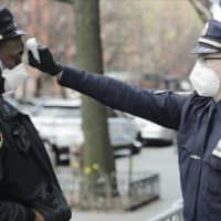 A police officer checks the temperature of all people entering the 32nd precinct of the New York Police Department in an attempt to stem the spread of the new coronavirus on Wednesday. | AP