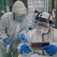 Medical workers check information as they take swab samples from people to be tested for COVID-19 in Wuhan on Thursday.  | AFP-JIJI