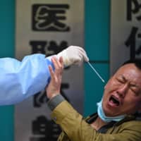 A man being tested for COVID-19 reacts as a medical worker takes a swab sample in Wuhan, China, on Thursday.  | AFP-JIJI