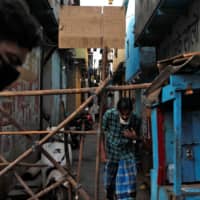 Men walk past a makeshift barricade meant to stop people from entering an area on April 9 during a nationwide lockdown in India to slow the spread of COVID-19, in Dharavi, one of Asia\'s largest slums. | REUTERS