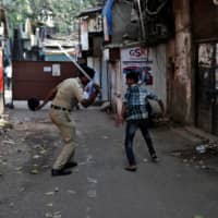A policeman wields his baton toward a man for breaking curfew during a nationwide lockdown in India on April 11. | REUTERS 