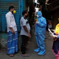 A doctor wearing a hazmat suit and a mask checks the temperatures of residents with an infrared thermometer, in Dharavi on April 11. | REUTERS