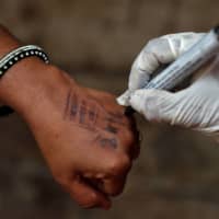 A health worker writes a date on a man\'s hand informing him of how long he should quarantine at home after he tested positive for COVID-19 in Dharavi on April 10.  | REUTERS 