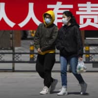 People walk in front of a propaganda billboard reading \"it is everyone\'s responsibility to control the spread of disease\" at a public park in Beijing on Tuesday.  | AP