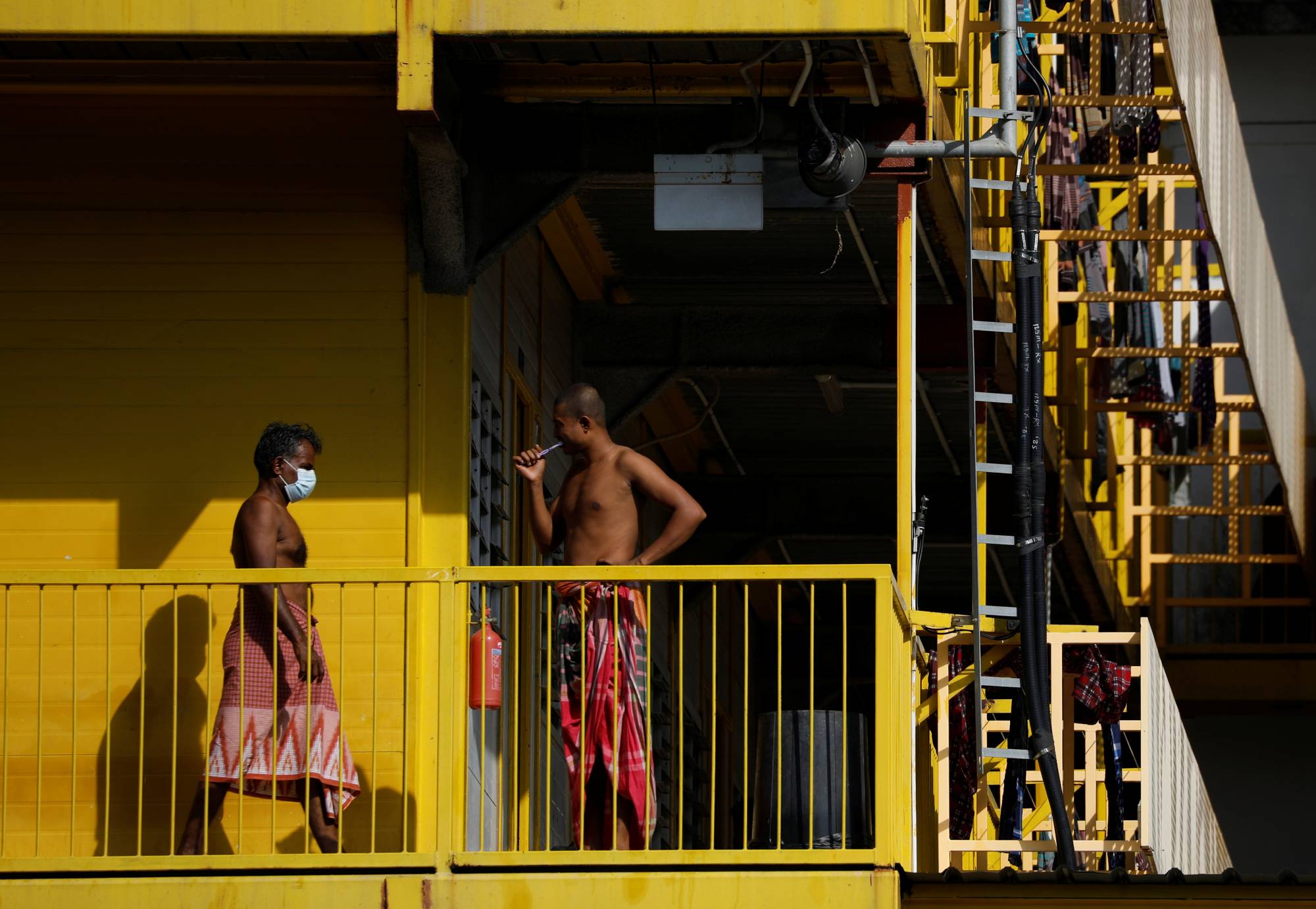 Migrant workers stand outside their rooms at a dormitory in Singapore on Tuesday. | REUTERS