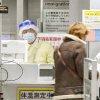 An official in protective gear at Narita Airport checks passengers arriving from South Korea on March 9. | KYODO
