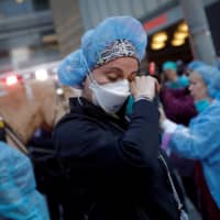 A nurse wipes away tears outside NYU Langone Medical Center in Manhattan as police officers cheer and thank health care workers last Thursday.  | REUTERS 