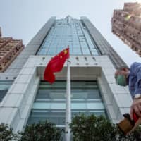A pedestrian walks past the Chinese flag flying outside the Liaison Office of the Central People\'s Government in the Sai Ying Pun district of Hong Kong on Monday.  | BLOOMBERG 