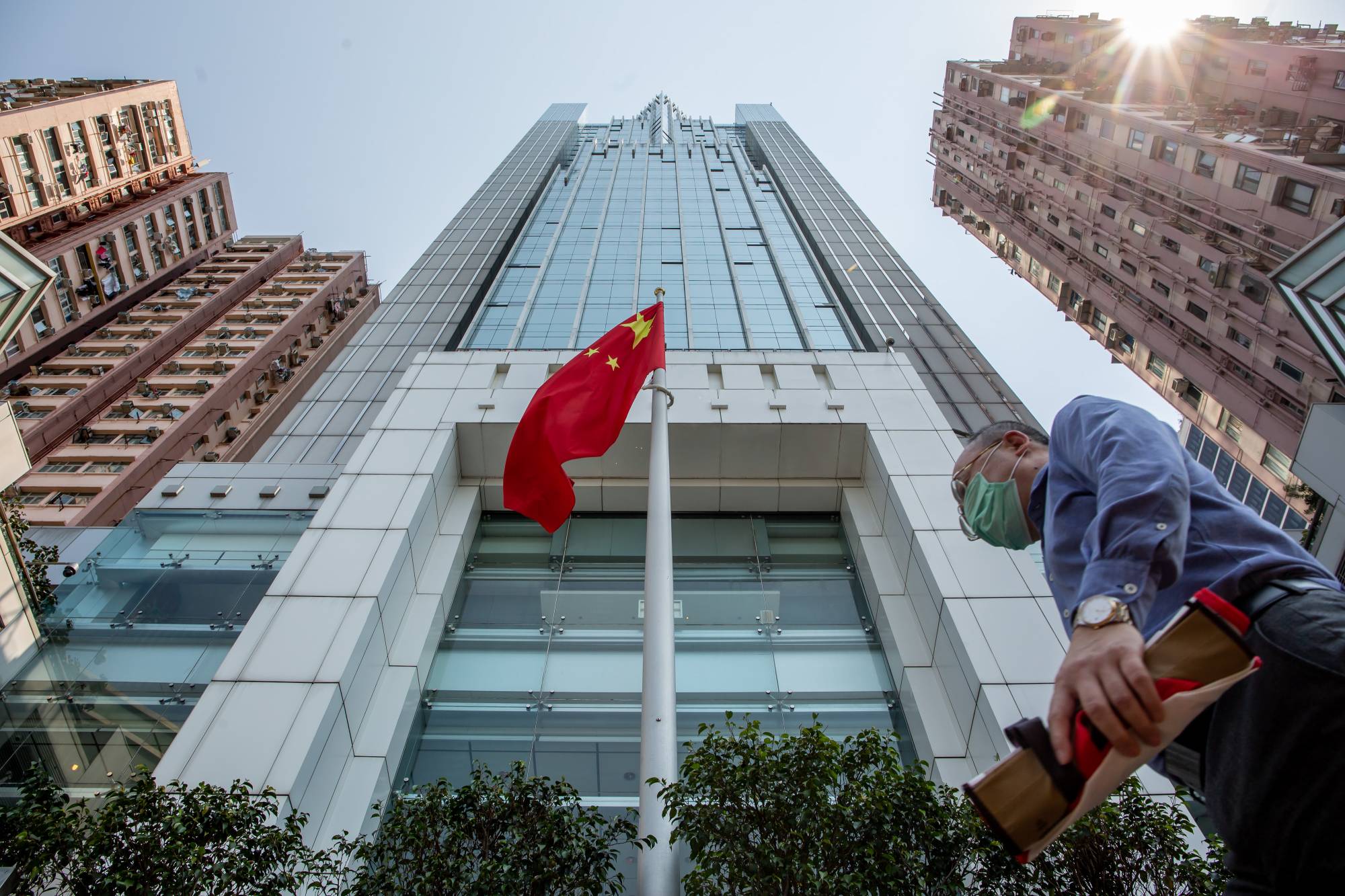 A pedestrian walks past the Chinese flag flying outside the Liaison Office of the Central People's Government in the Sai Ying Pun district of Hong Kong on Monday. | BLOOMBERG 