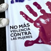 A woman stands next to a banner reading \"No More Violence Against Women\" before the start of a march to protest against violence against women in Lima, Peru, in August 2017. The lockdown in countries around the world as a measure against the spread of the new coronavirus has escalated help requests from victims of domestic abuse. | AFP-JIJI