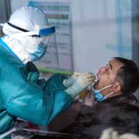 Medical personnel taking swab samples of a man for testing as part of COVID-19 pandemic measures, at a health services center in Suifenhe, China, on Friday. | AFP-JIJI