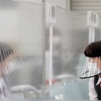 A staff member wearing a face shield talks to a bank teller at a counter where a plastic curtain is installed in order to prevent infections following the COVID-19 outbreak, at the Higashinakano branch of MUFG Bank in Tokyo on Friday. | REUTERS 
