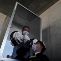 A medical worker conducts a simulation for a walk-in style test for COVID-19 on Thursday at a makeshift facility in Yokosuka, Kanagawa Prefecture. | REUTERS