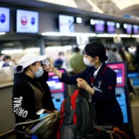 A Japan Airlines employee scans the temperature to a passenger at the almost empty Kansai International Airport in Osaka on March 14. | REUTERS