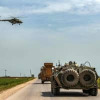 A Russian Air Force Mil Mi-28 military helicopter flies over Turkish and Russian military vehicles taking part in a joint Turkish-Russian patrol outside the Syrian town of Darbasiyah near the Turkish border in the province of Hasakah, on April 22. | AFP-JIJI