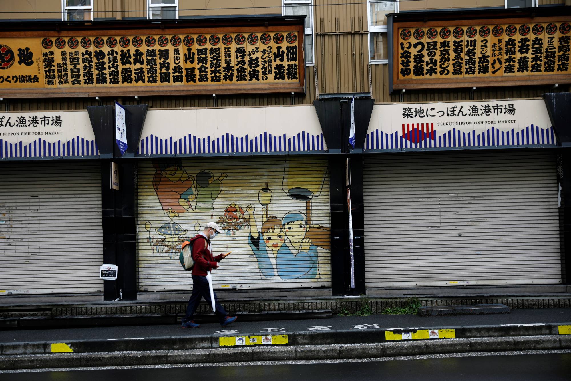 A man wearing a protective face mask walks past closed shops at Tsukiji market in Tokyo on Tuesday. | REUTERS