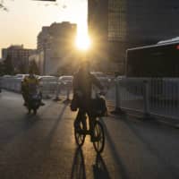 Cyclists ride along a road as the sun sets in Beijing on April 23. With Chinese experts concluding that the virus cannot be eradicated, government officials are focused on keeping infections to a manageable level to avoid catastrophic surges that overwhelm hospitals. | BLOOMBERG
