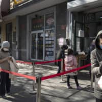 Customers wearing protective masks use social distancing markers at the entrance to a store selling steamed buns in Beijing on April 23. | BLOOMBERG