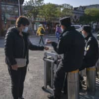 A security official checks the temperature of a pedestrian wearing a protective mask at a checkpoint in the Dashilan area of Beijing on April 23.  | BLOOMBERG