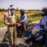 A police officer wearing a protective mask questions a motorcyclist at a checkpoint during a partial lockdown in Uttar Pradesh, India, on April 21. The federal government has made a series of moves that has eroded the ability of states to raise the cash needed to handle the coronavirus. | BLOOMBERG