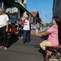 People soak up some sun in Jakarta on April 17. Some central banks in the developing world, like Bank Indonesia, are buying sovereign debt directly, taking a step further even than most developed-economy peers. | AFP-JIJI
