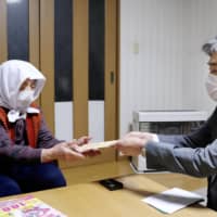 A local government official in Aomori Prefecture distributes a one-off government handout of ¥100,000 to a woman in Nishimeya village on Thursday to help deal with the coronavirus pandemic. | KYODO