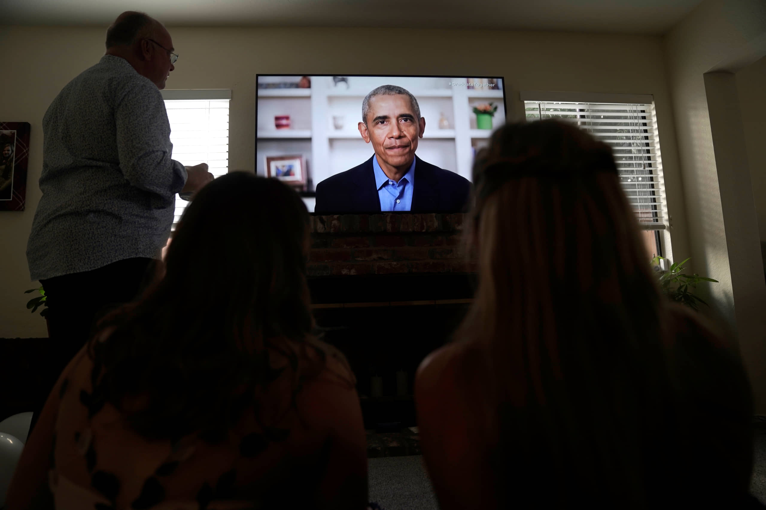 Torrey Pines High School graduating student Phoebe Seip, 18 (right), her father, Jake, 57, and her sister, Sydney, 22, watch former U.S. President Barack Obama deliver a virtual commencement address to millions of high school seniors who will miss graduation ceremonies due to the coronavirus pandemic, while celebrating Phoebe's canceled prom night at home in San Diego on Saturday. | REUTERS