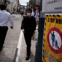 People walk on a street next to a \"stay home\" notice as a preventive measure against coronavirus in Tokyo on May 12. | AFP-JIJI