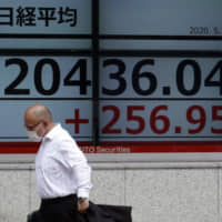 A man wearing a face mask walks past an electronic stock board outside a securities firm in Tokyo as temperatures in the capital and across Japan soared Monday, with many areas in the Kanto region topping 30 degrees Celsius — levels on par with those of midsummer days. | AP