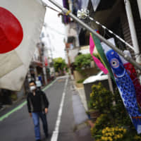 A man with a face mask walks near a Japanese national flag and colorful carp streamers to celebrate Children\'s Day on Tuesday in Tokyo. | AP