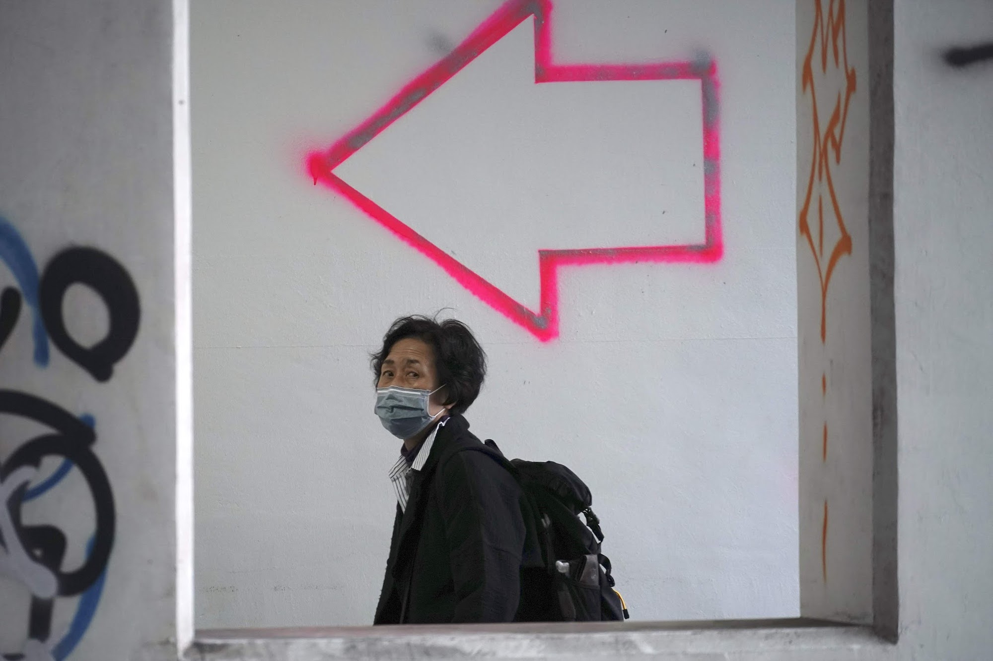 A woman wearing a mask walks past graffiti in Tokyo on Friday. Ahead of schedule, Japan lifted the state of emergency in the Tokyo metropolitan area and in Hokkaido  on Monday.  | AP
