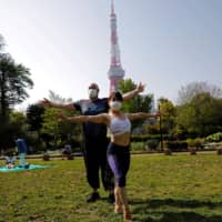 People wear protective face masks as they perform acroyoga at a park next to Tokyo Tower, amid the coronavirus outbreak, in Tokyo on Saturday. | REUTERS