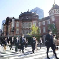 Commuters wearing face masks walk in front of Tokyo Station on Thursday morning, the first workday after the Golden Week holiday. | KYODO