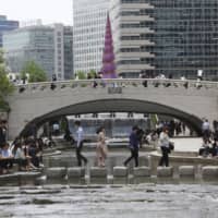 People relax at the Cheonggye Stream as daily life slowly returns to normal amid a lifting of restrictions in the wake of the coronavirus pandemic in Seoul on Thursday. | AP