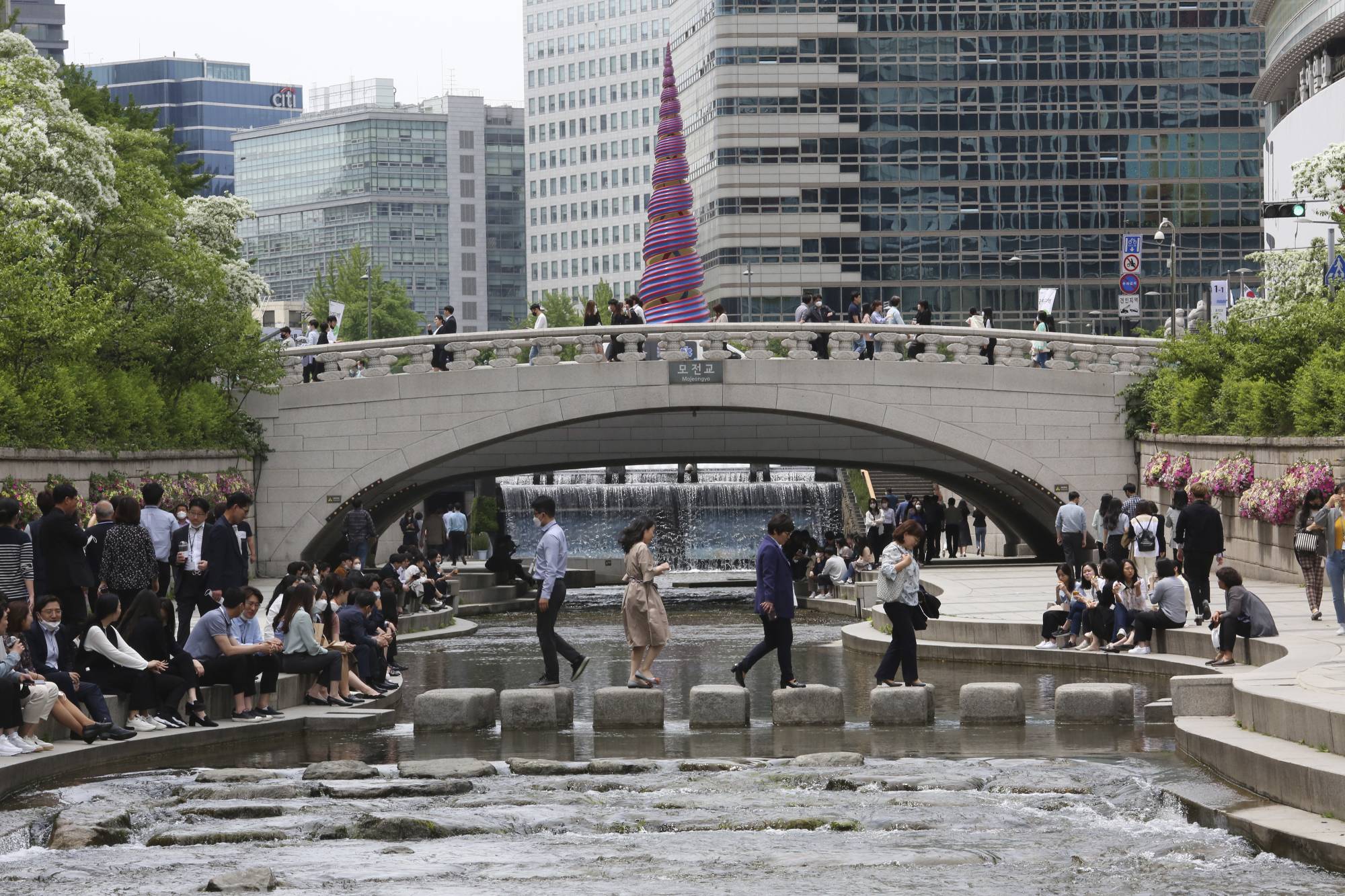 People relax at the Cheonggye Stream as daily life slowly returns to normal amid a lifting of restrictions in the wake of the coronavirus pandemic in Seoul on Thursday. | AP