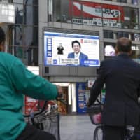 People watch a news conference by Prime Minister Shinzo Abe in which he explained the extension of a nationwide state of emergency over the coronavirus pandemic until the end of the month, in Osaka\'s Dotonbori district on May 4.  | KYODO