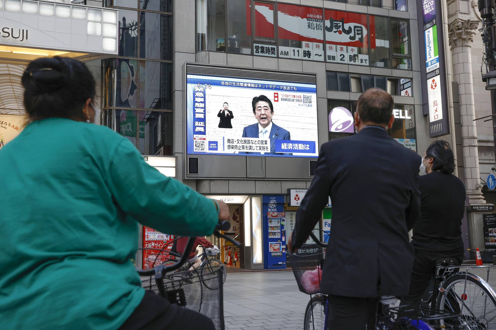 People watch a news conference by Prime Minister Shinzo Abe in which he explained the extension of a nationwide state of emergency over the coronavirus pandemic until the end of the month, in Osaka's Dotonbori district on May 4.  | KYODO