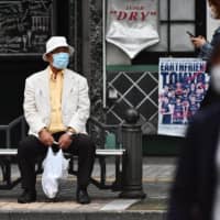 An elderly man wearing a face mask sits on a bench while people walk in a street amid the COVID-19 coronavirus outbreak in Tokyo on Sunday. | AFP-JIJI