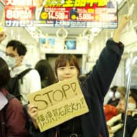 Yui Tanaka, 20, holds a sign that reads \"Stop coal power in Yokosuka!\" on her way to a protest at the construction site of a new coal power plant in the city in March. | RYUSEI TAKAHASHI

