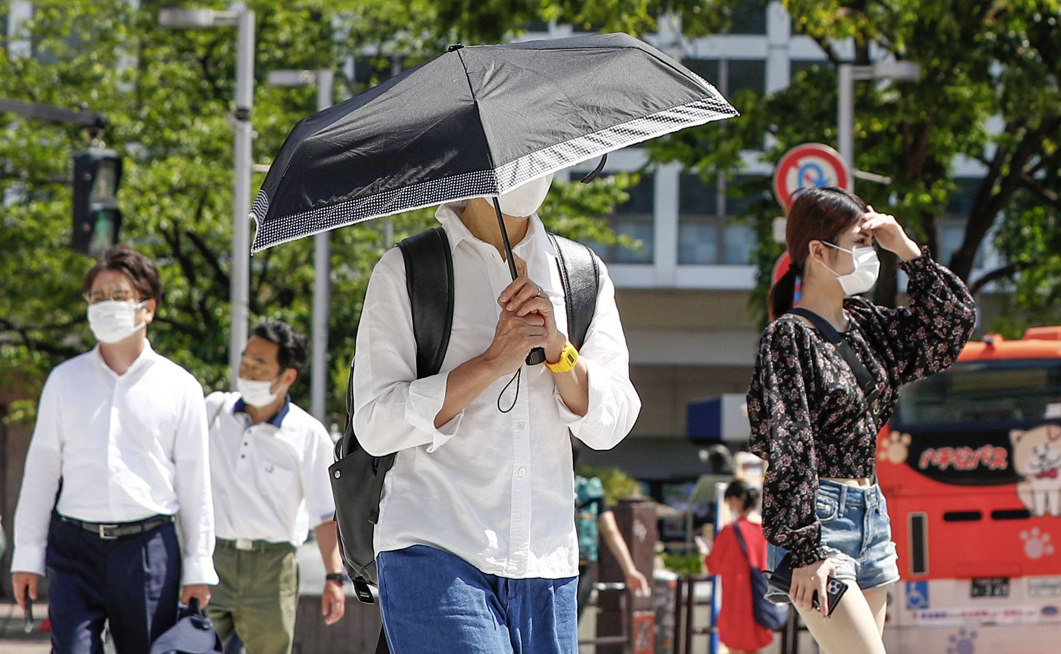 People wearing face masks walk in unseasonably hot weather in Tokyo on Monday. | KYODO