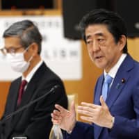 Prime Minister Shinzo Abe gestures as he speaks alongside Shigeru Omi, president of the Japan Community Healthcare Organization, during a news conference in Tokyo on May 4. | BLOOMBERG