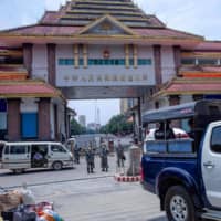 Chinese border police keep watch as migrant workers return from China at the Myanmar border gate in Muse, Shan state, on Tuesday.  | AFP-JIJI